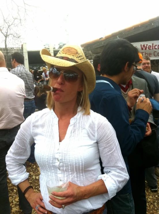 a woman in a straw hat holds her drink while standing next to a group of people