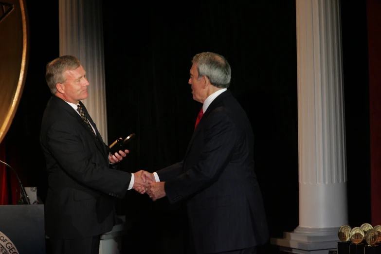 two men in suits shaking hands while another man stands nearby