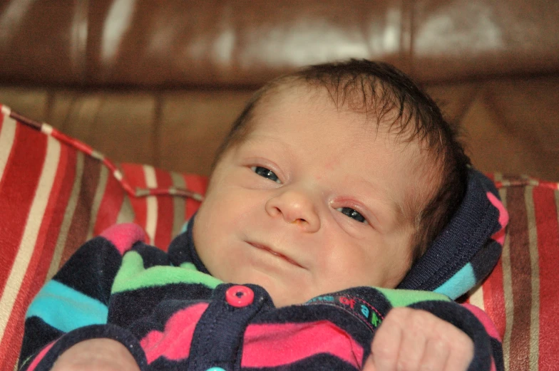 a baby in a bright colorful outfit with a striped blanket on a couch