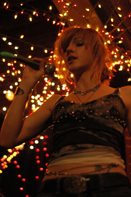 a blonde woman in front of christmas lights singing into a microphone