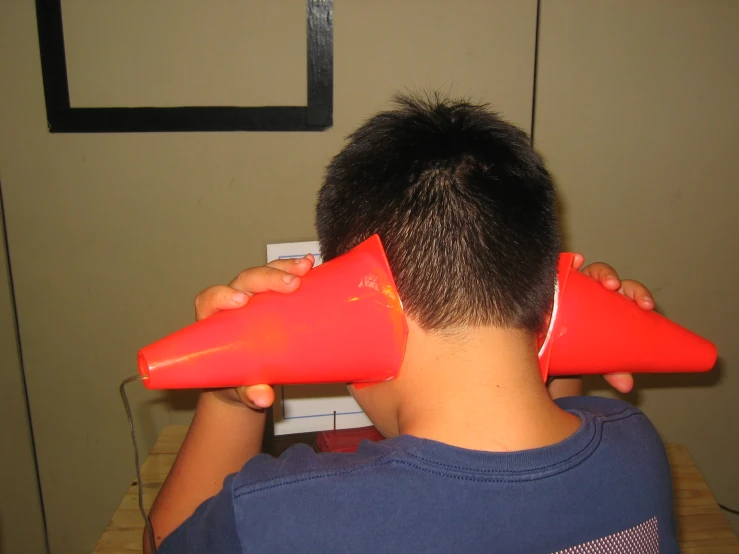 a  holds two red cones up to his head