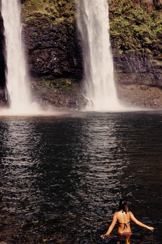 a woman with a small child stands in the water near waterfall