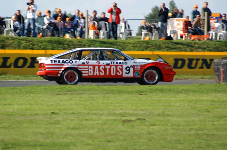 an old race car driving on a track with fans watching from stands