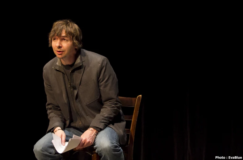 the man is sitting on a chair talking into a microphone