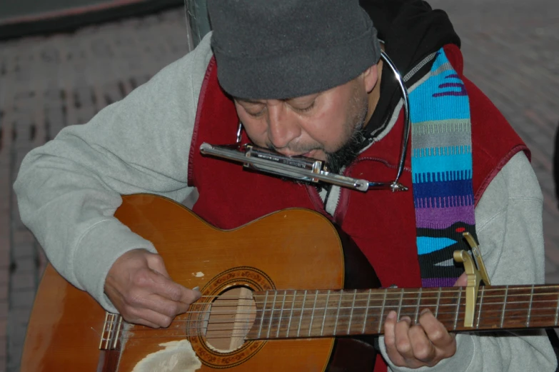 man with red vest playing guitar on cobblestone area