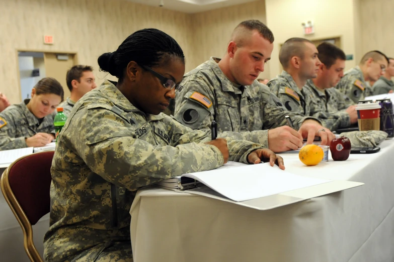 some soldiers in military fatigues sit at a long table and prepare to write