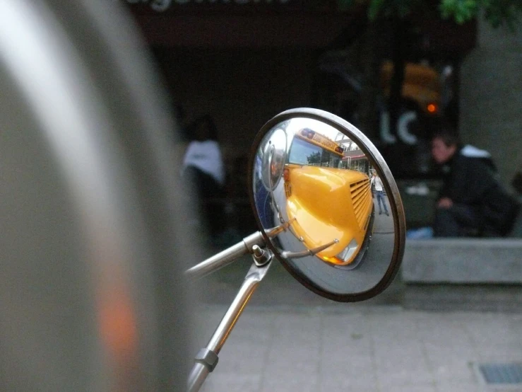 a side view mirror on a motorcycle with people sitting in the background