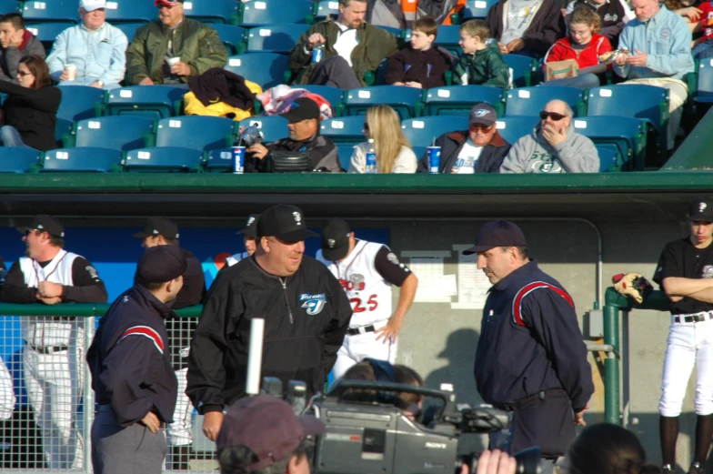 two men in black jackets and baseball uniforms stand together as people walk up and down the sidelines