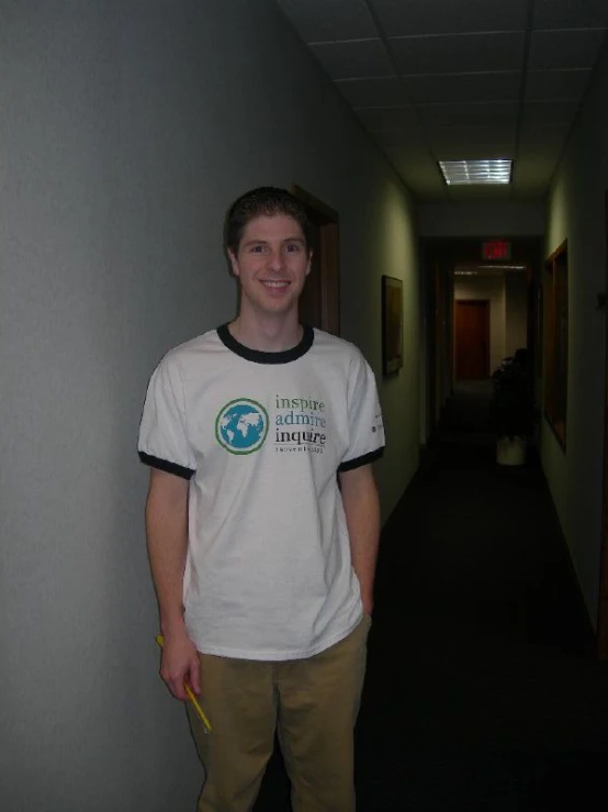 a man standing in an empty hallway wearing a shirt and khaki pants