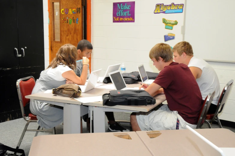 four students with laptops at a desk with chairs