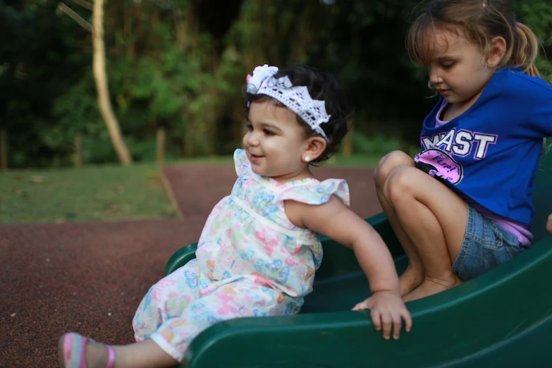 two little girls sitting in a green park play structure