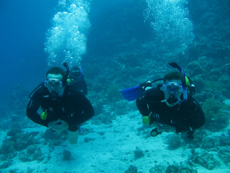 two scubaiers wearing helmets and scuba gear are observing the bottom of a coral