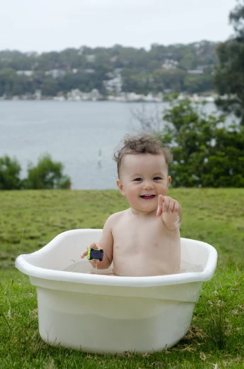 a baby sits in a tub and holds his thumb up to the camera