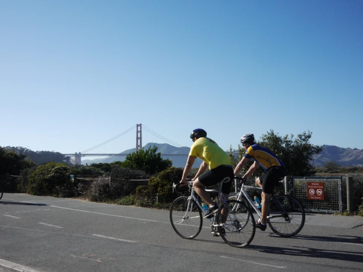 two bicyclists riding the road near some tall hills