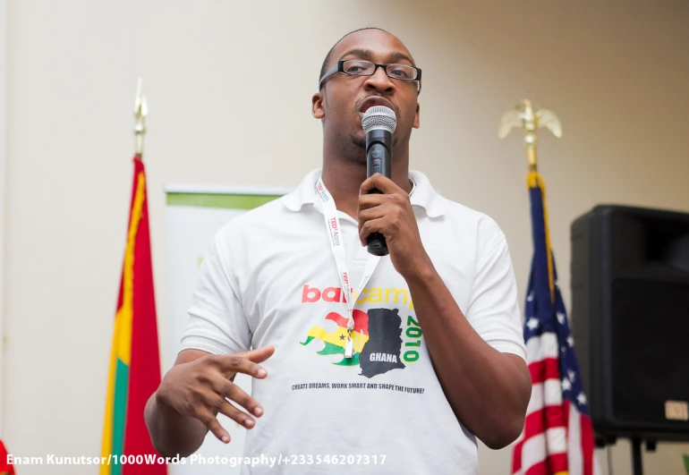 a black man speaking into a microphone and several american flags