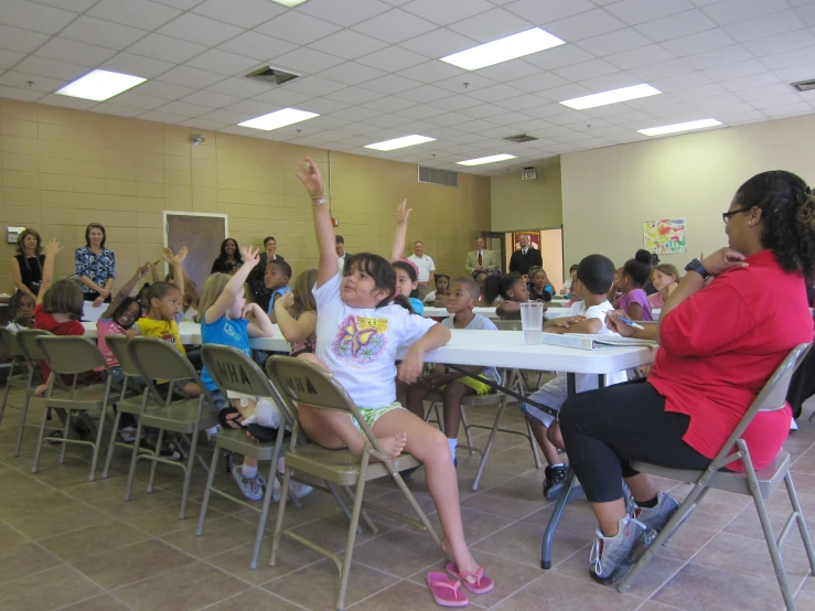 a group of children sitting at tables and listening to adults