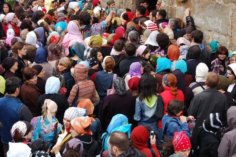 a large crowd of people stand next to a rock wall