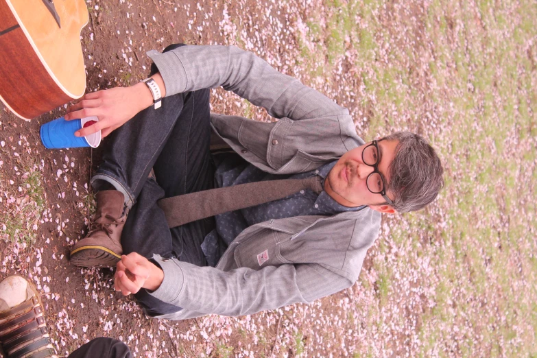 a man sits with a blue cup and brown guitar in front of him