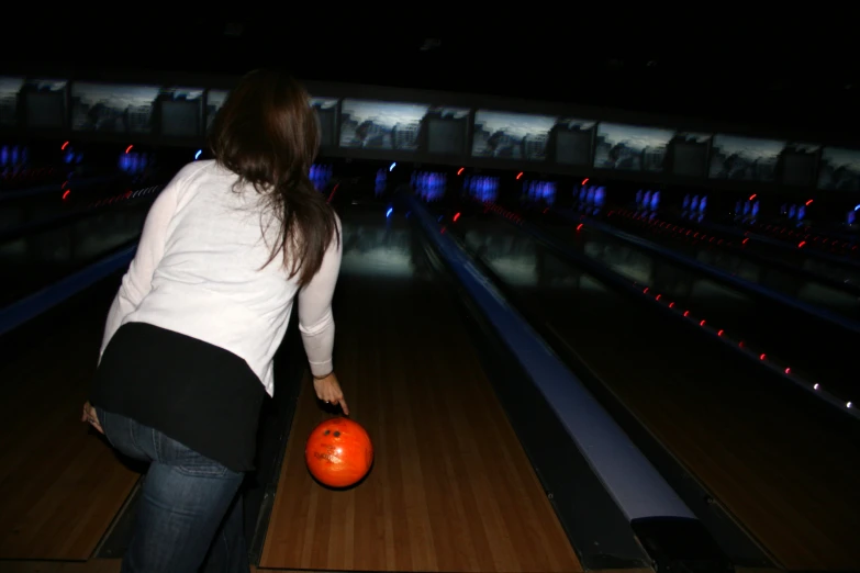 a woman is standing with an orange ball at a bowling alley