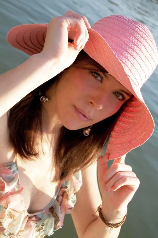 a girl in a pink hat sitting by the water