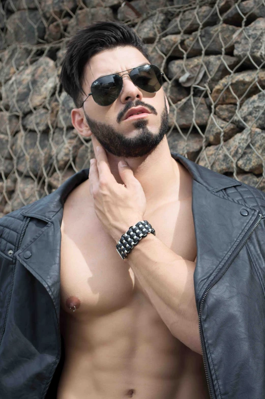 a man with dark glasses posing against a rock wall