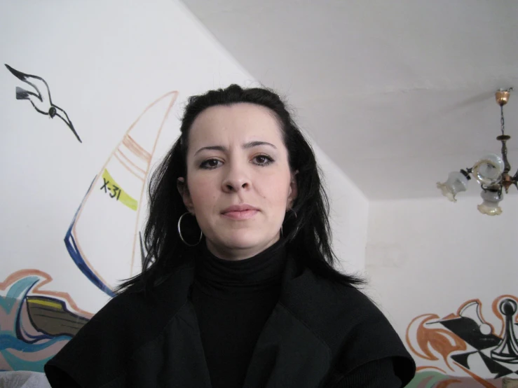 the woman has long hair and black clothing in front of a wall with paintings