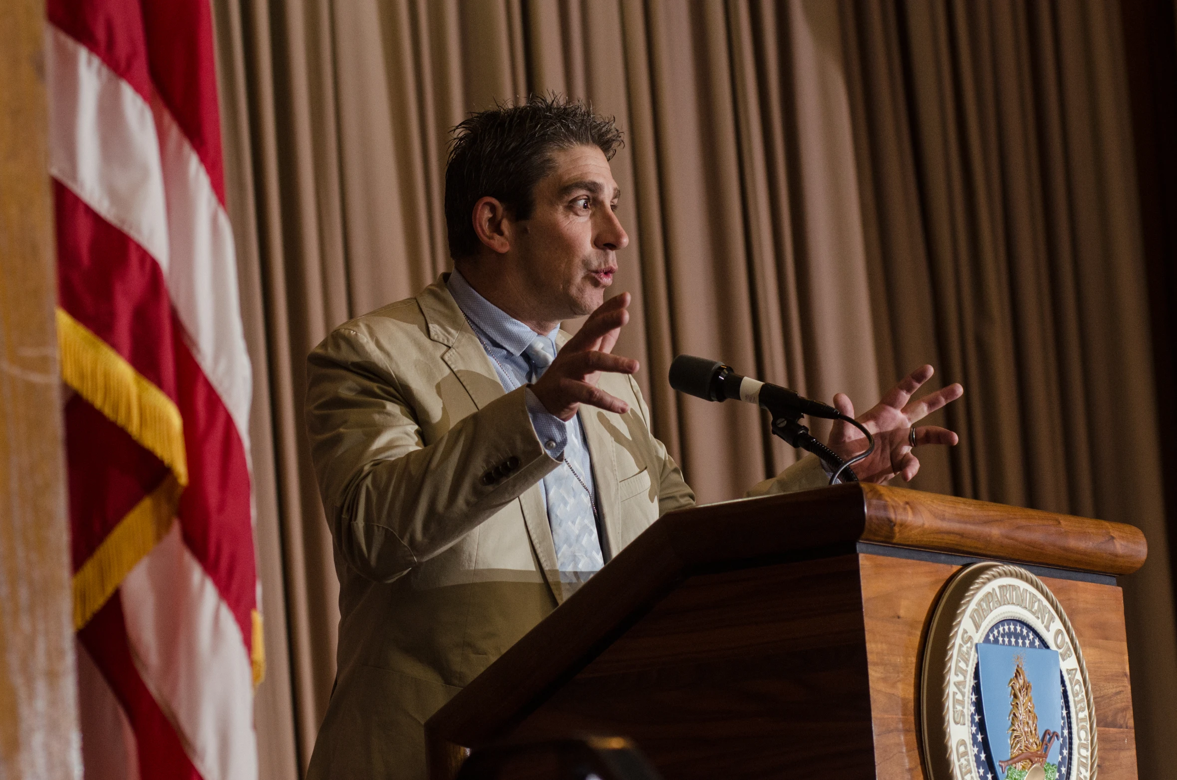 man speaking at podium during press conference next to flags