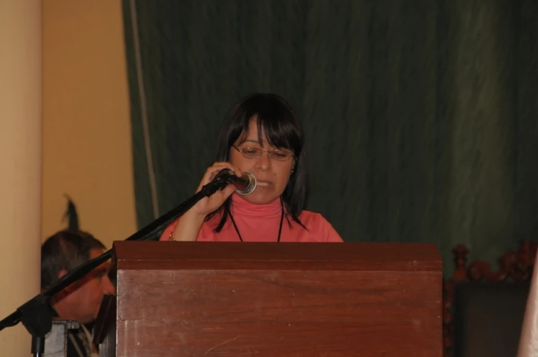 a woman in pink shirt holding a microphone and talking on a cell phone