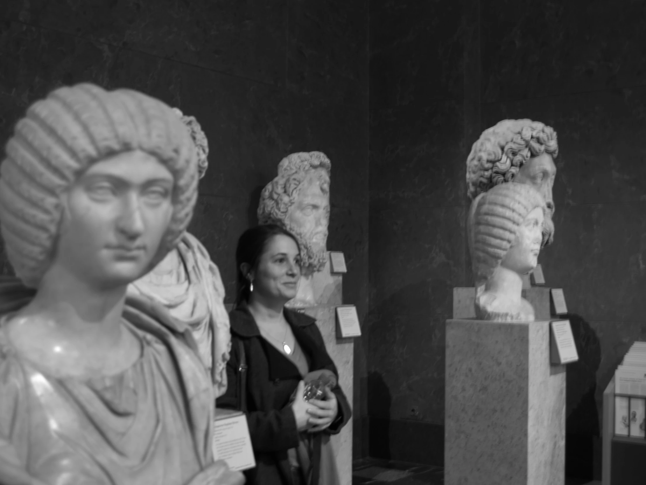 a woman standing near two busts with heads down