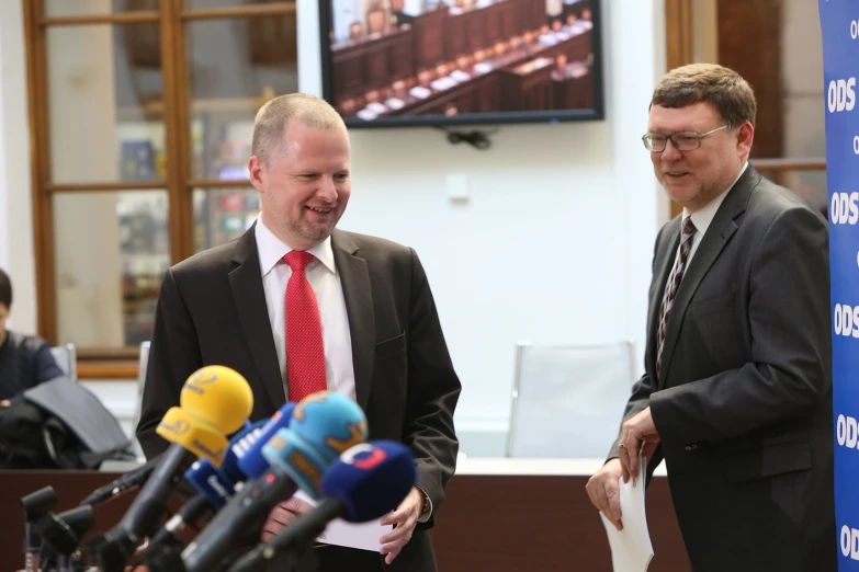 two men in business suits stand by microphones talking