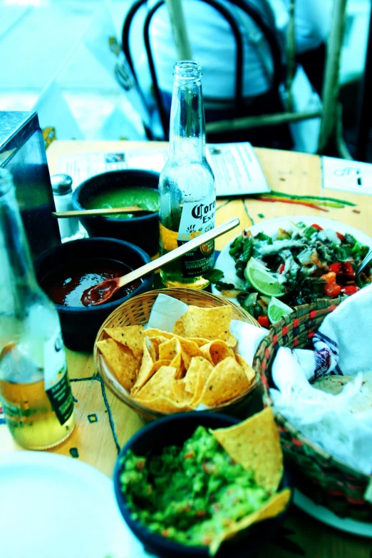 a table with some guacamole, salsa, chips and beer