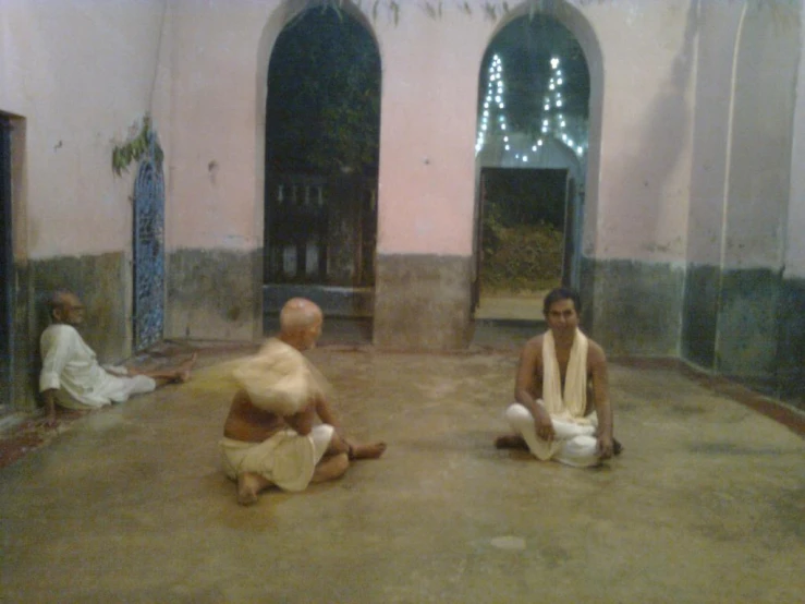 two men sit on the ground in front of some archways