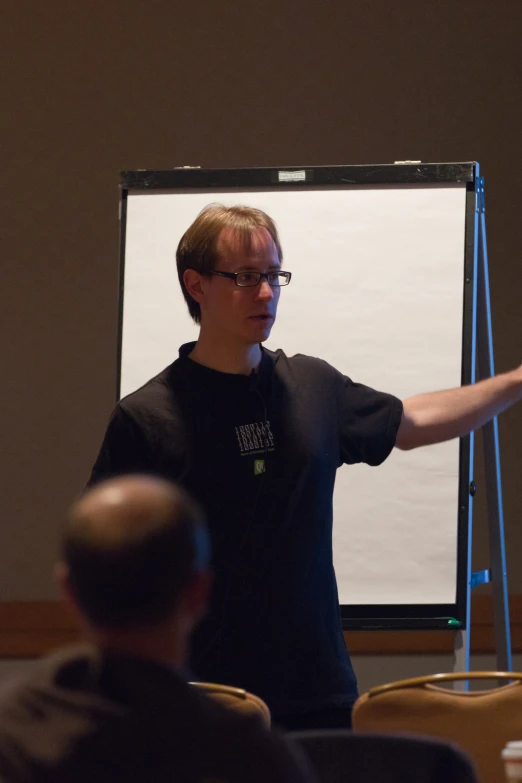 man with glasses holding out his hand while standing in front of screen