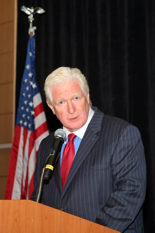 an old man in business attire at a podium