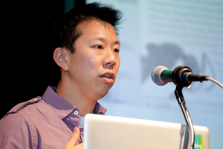 a man speaking on stage with a laptop