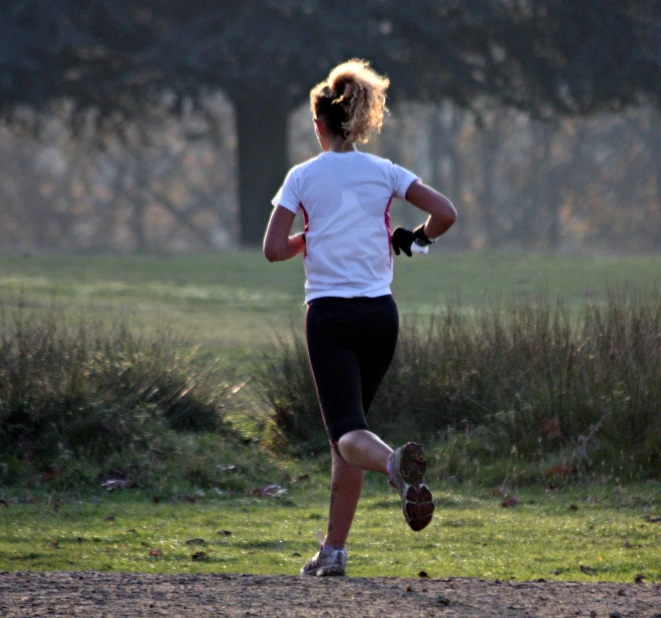 a woman running through a field wearing baseball gloves