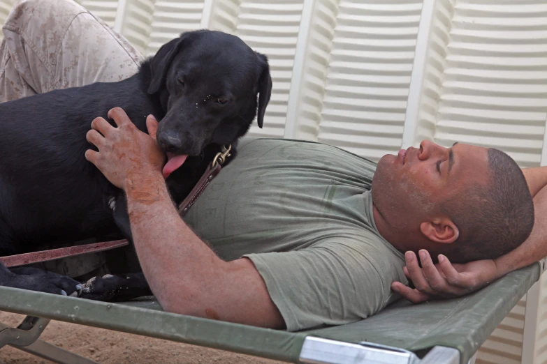 a man lays down on a bench with a large black dog