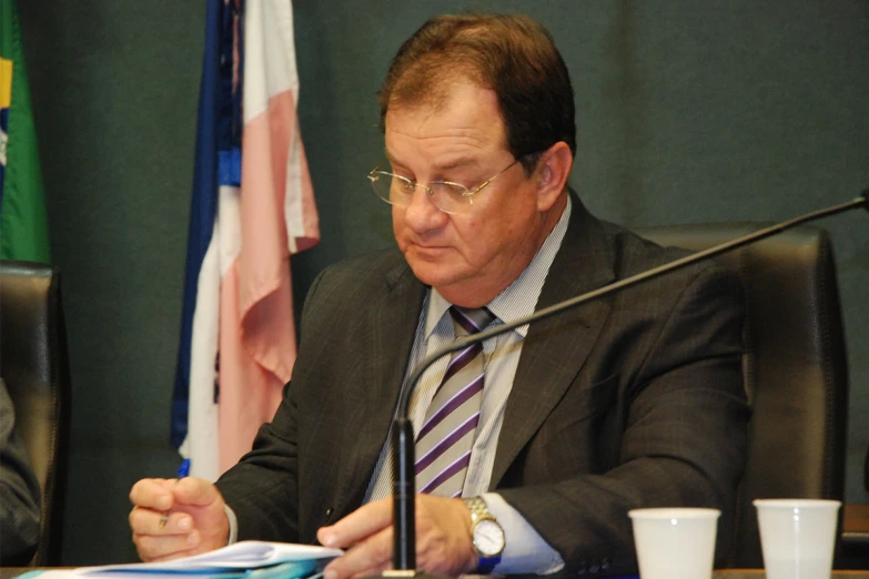 a man wearing glasses sitting in front of a table holding papers