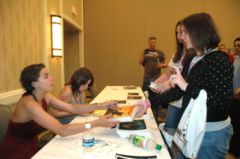 three people seated at tables while a third woman holds soing in her hand