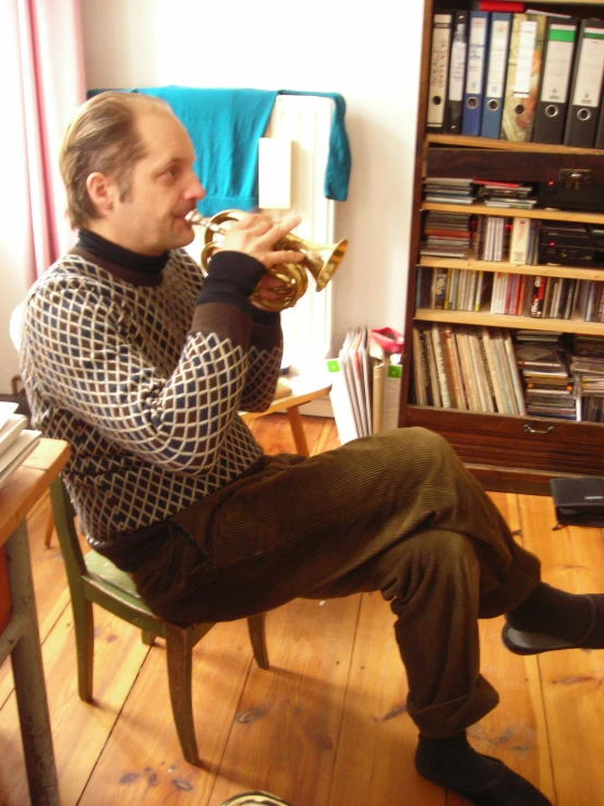 man sitting on chair playing trumpet next to bookshelf