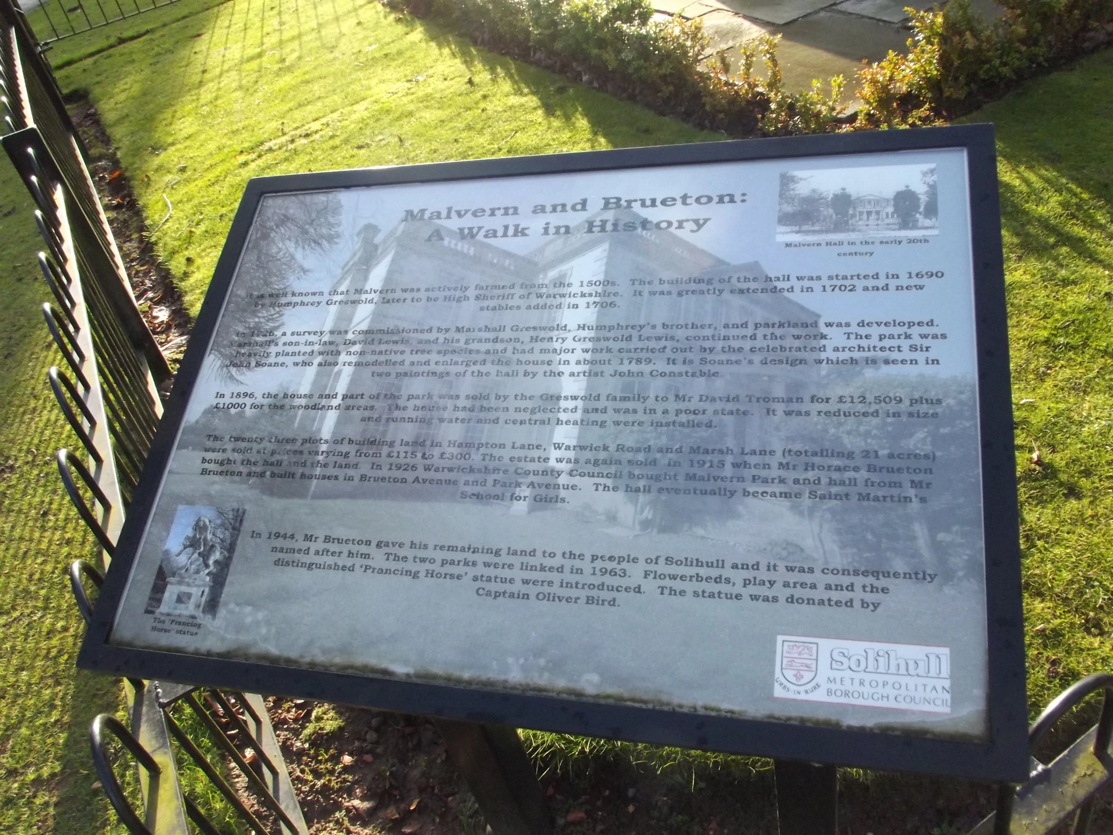 an information plaque in the grass behind a gate with writing in it