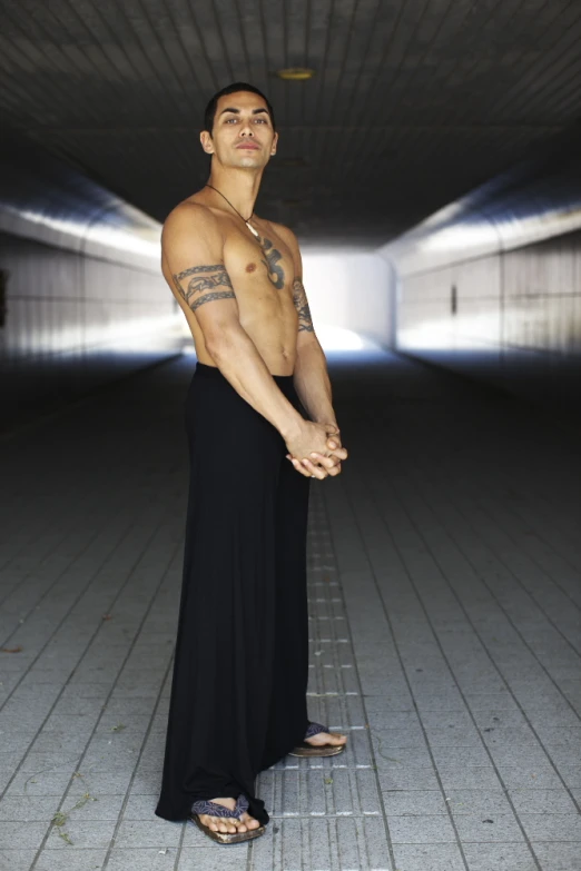 a man is posing in a long skirt and shirtless