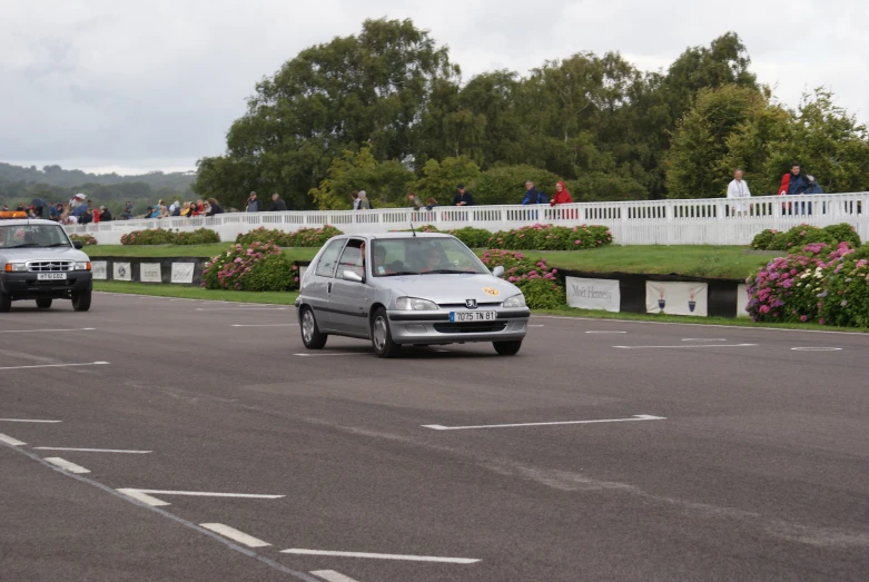 two cars driving down the road with people standing around them