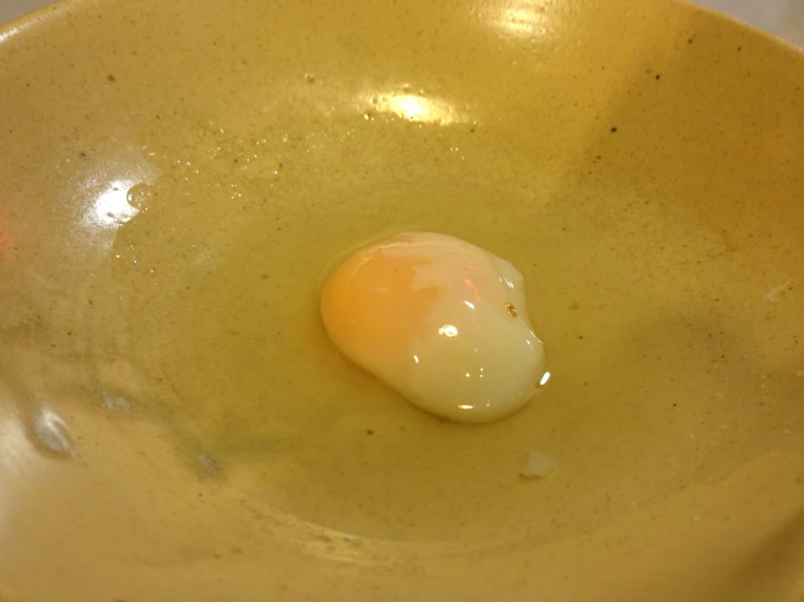 an egg sits in a yellow bowl on a table