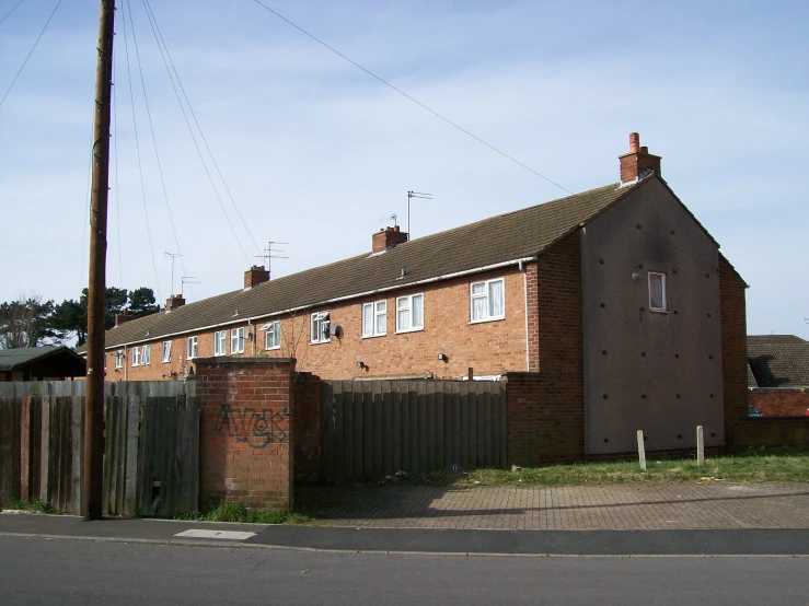 a brick building with a few chimneys near a fence and road