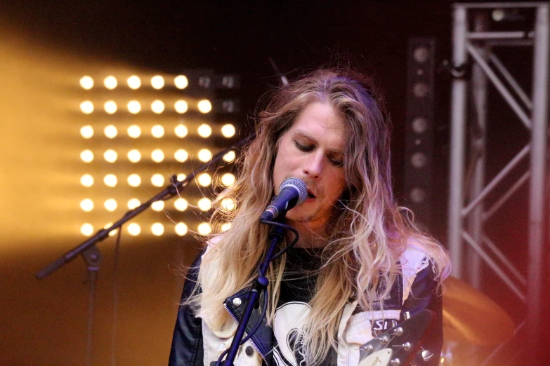 a blonde lady singing and playing guitar on stage