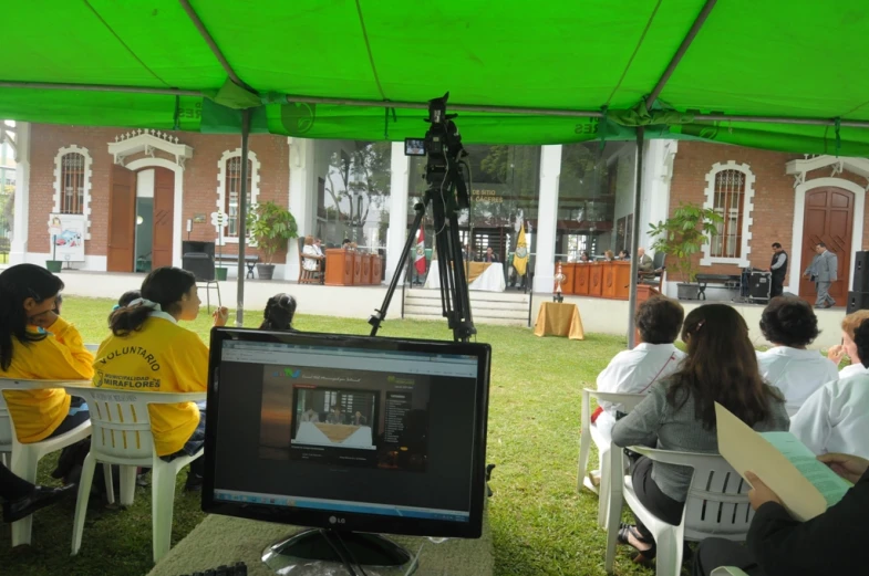 a crowd watches as people watch a camera and video screen