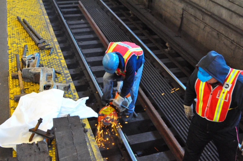 two men standing on tracks welding soing off of a locomotive