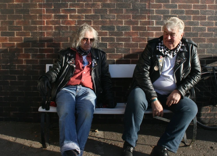 two people sit on a bench in front of a brick wall