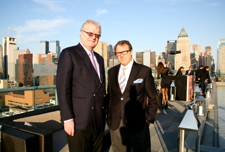 two people in suits and sunglasses pose on a rooftop